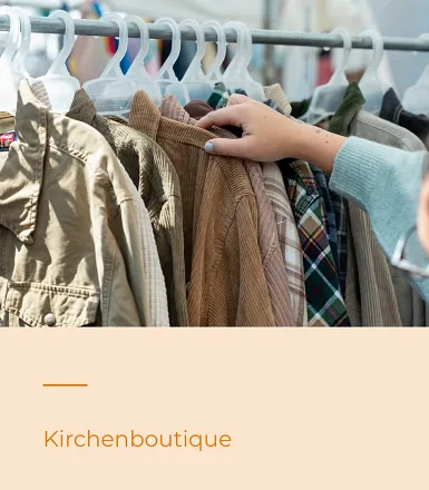 Ein Hand greift nach einem Kleidungsstück, das neben anderen Klamotten auf einer Kleiderstange hängt