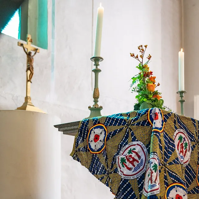 Altar der Dorfkirche Alt-Staaken mit brennenden Kerzen, Blumen und einem bunten Tuch der Partnerkirche in Tansania, daneben ein Kruzifix