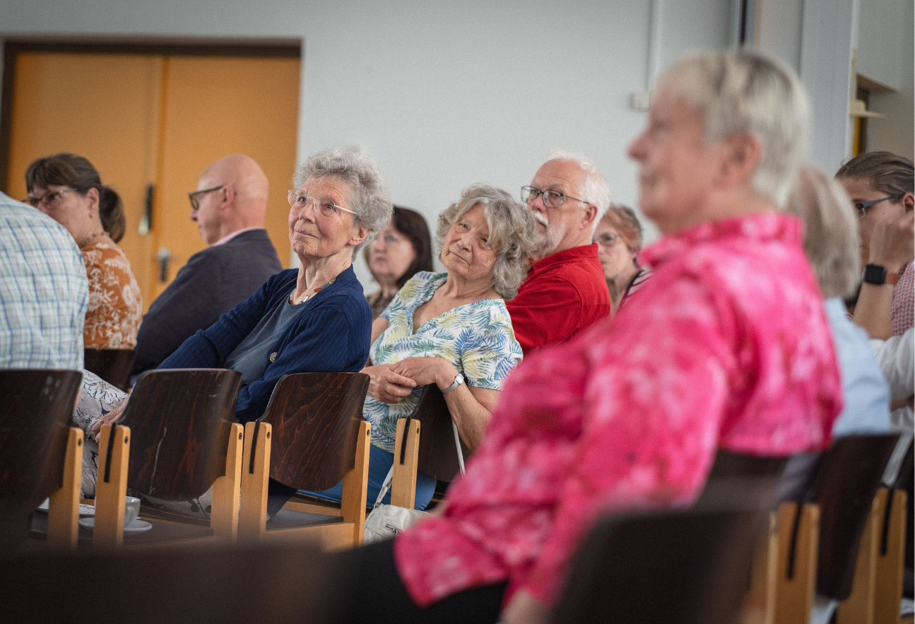 Mehrere Menschen sitzen im Publikaum und schauen gespannt zum Redner, der nicht im Bild ist