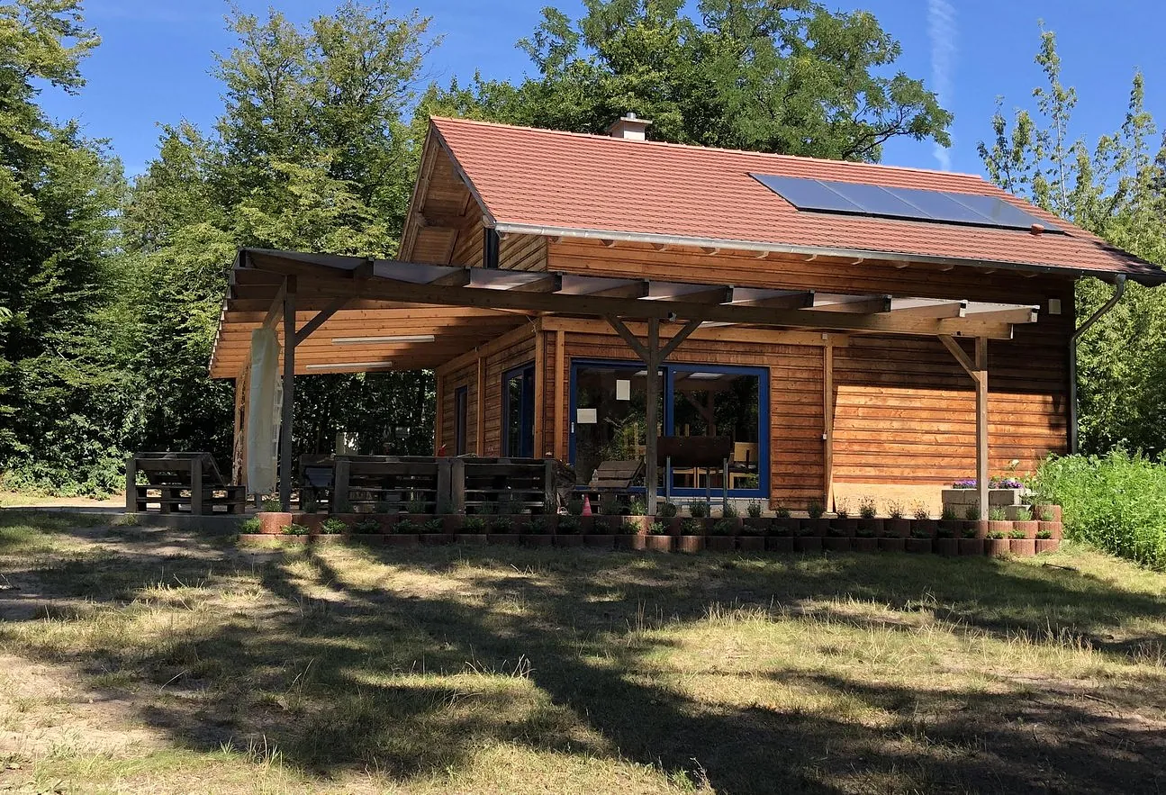 Waldhaus am Sonnenhügel: Holzhaus mit rotem Ziegeldach und überdachter Terrasse zwischen Bäumen