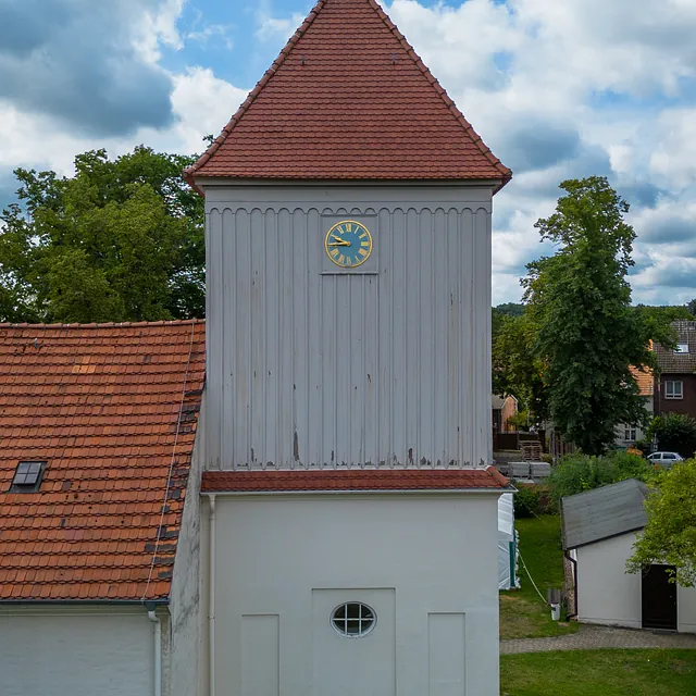 Kirchturm der Dorfkirche Alt-Staaken mit Uhr und Wetterfahne vor bewölktem Himmel