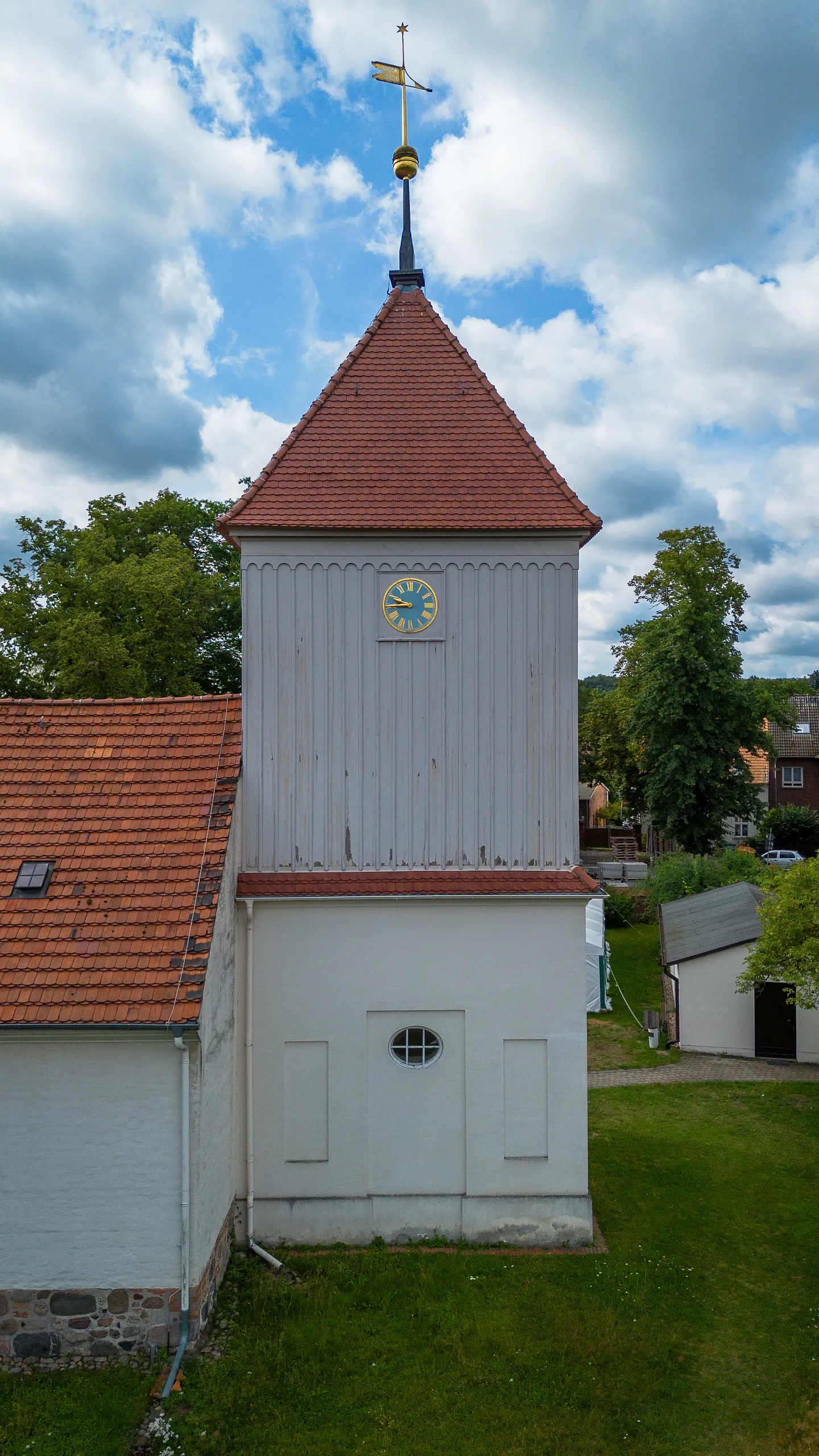 Kirchturm der Dorfkirche Alt-Staaken mit Uhr und Wetterfahne vor bewölktem Himmel
