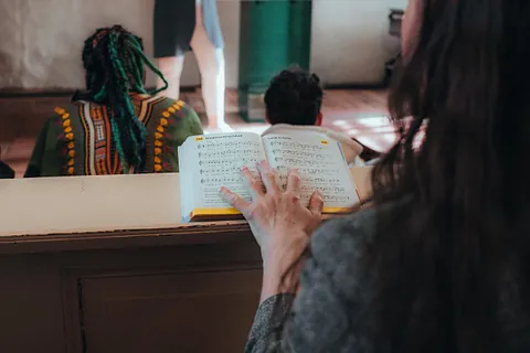 Gottesdienst von hinten gesehen: Eine Hand liegt auf einem aufgeschlagenen Liederbuch, davor sitzen Menschen in der Kirchenbank