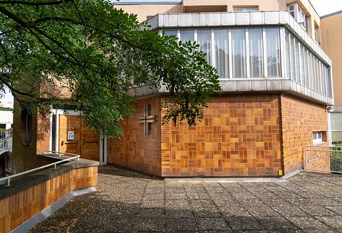 Kirche Heerstraße Nord: Klinkerfassade mit Kreuz im Gemeinwesenzentrum, davor ein Baum und ein gepflasterter Vorplatz