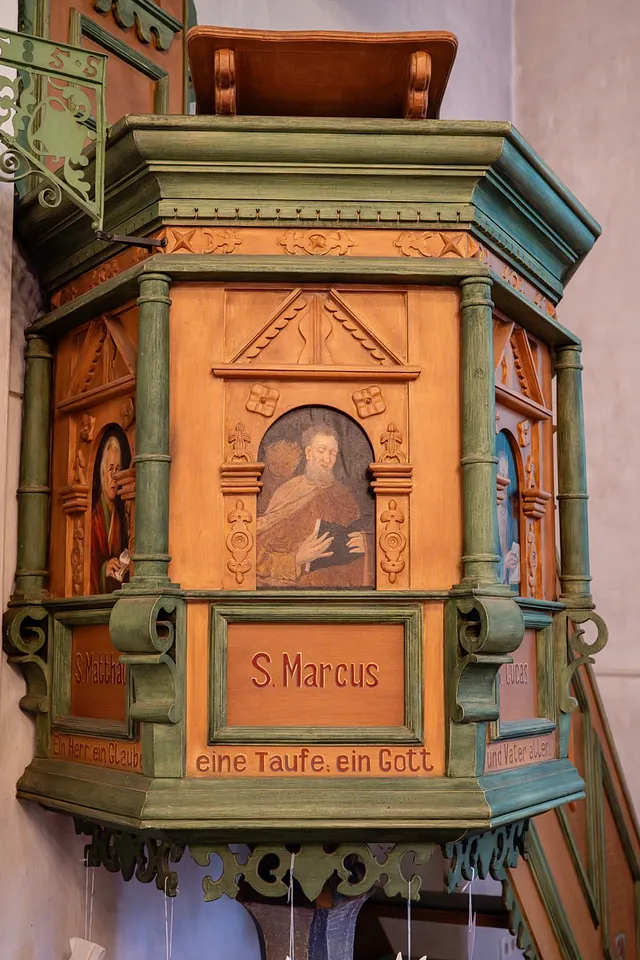 Detailaufnahme der historischen, reich verzierten Holzkanzel in der Dorfkirche Alt-Staaken. Zu sehen sind geschnitzte Ornamente, grün gefasste Säulen und Bildtafeln mit Darstellungen der Evangelisten.