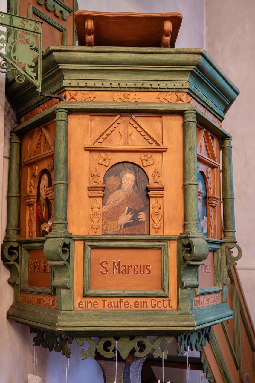 Detailaufnahme der historischen, reich verzierten Holzkanzel in der Dorfkirche Alt-Staaken. Zu sehen sind geschnitzte Ornamente, grün gefasste Säulen und Bildtafeln mit Darstellungen der Evangelisten.