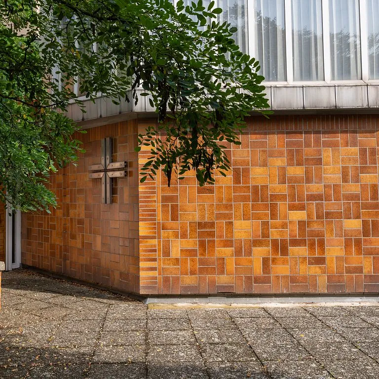 Fassade des Kirchraums mit Kreuz und orangebraunen Fliesen