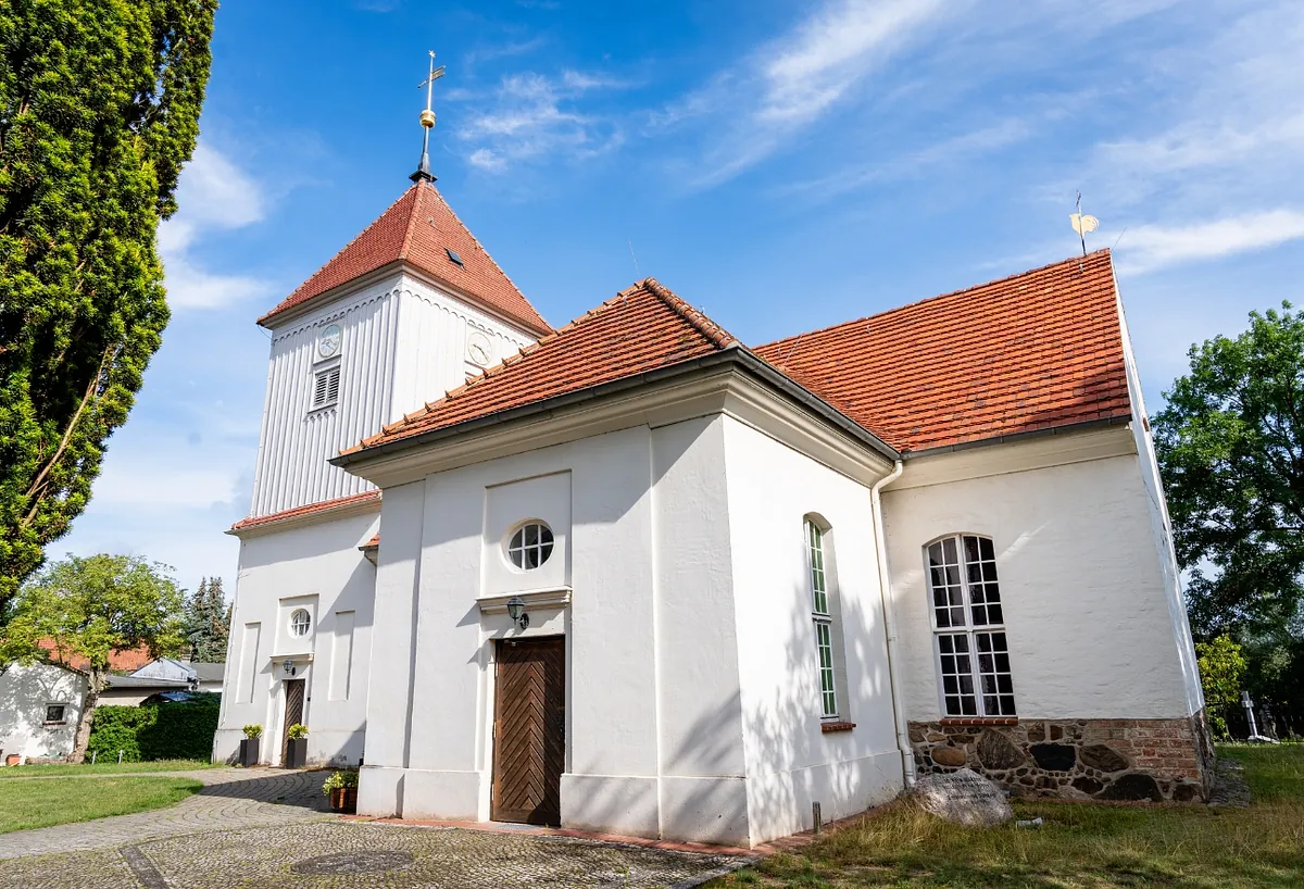 Weiße Dorfkirche Alt-Staaken mit rotem Ziegeldach und Kirchturm vor blauem Himmel