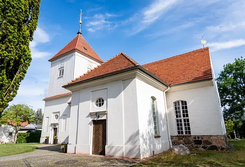 Weiße Dorfkirche Alt-Staaken mit rotem Ziegeldach und Kirchturm vor blauem Himmel
