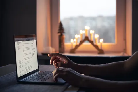 Hände an einem Laptop mit geöffnetem Newsletter, im Fenster dahinter leuchtet ein Schwibbogen