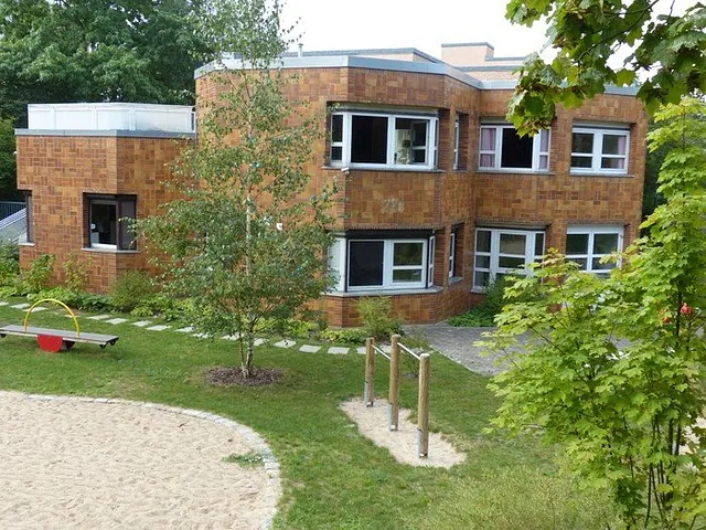 Zweigeschossiges Kitagebäude der Kita Regenbogen mit Klinkerfassade, davor Garten mit Sandweg und Klettergerüst