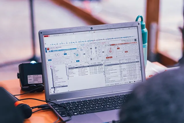 Laptop mit DJ-Software auf einem Tisch bei einem Fest im Freien, davor Mikrofon und Lautsprecher