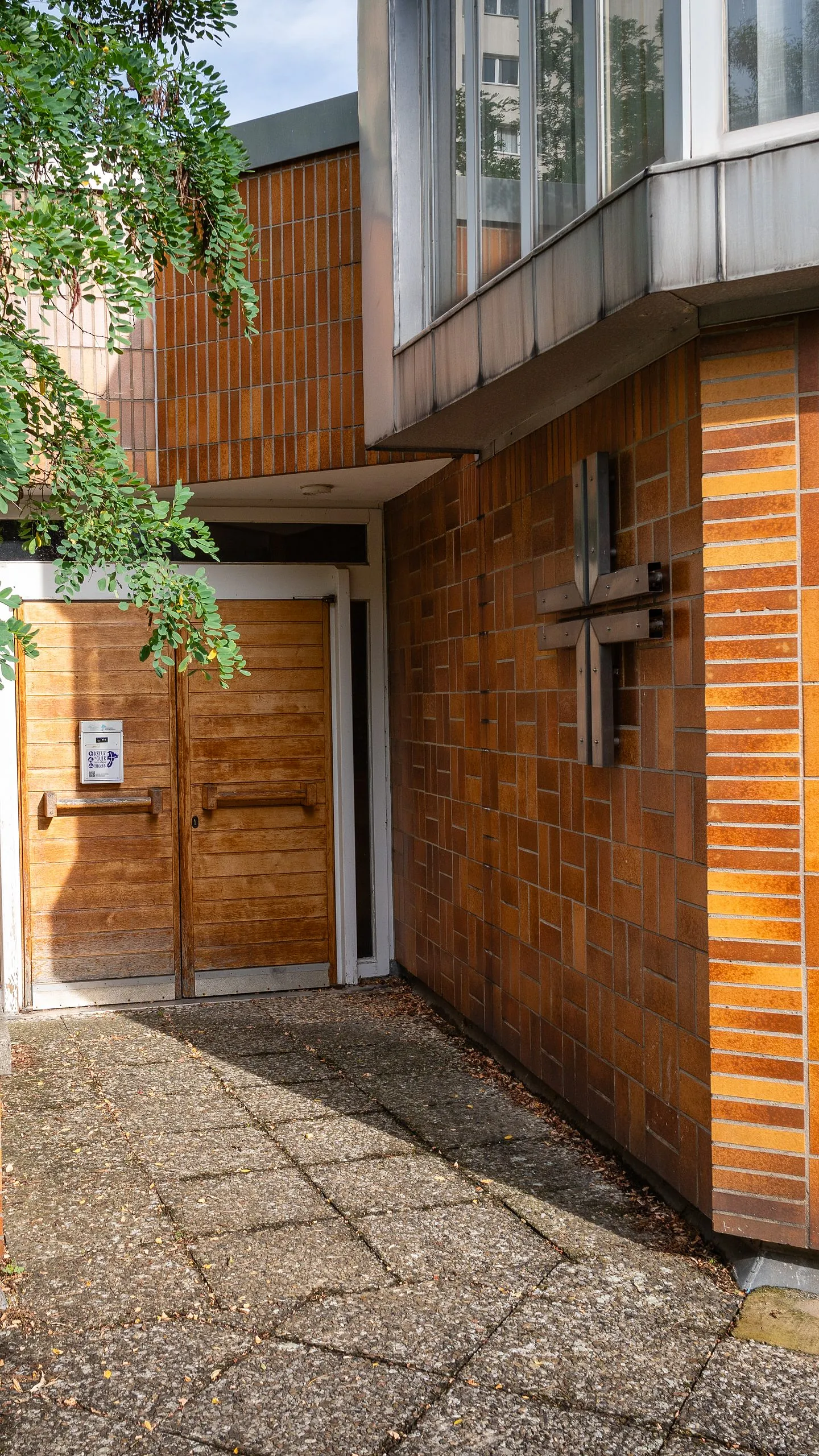 Eingang der Kirche Heerstraße Nord mit Holztür und Kreuz an der Klinkerwand