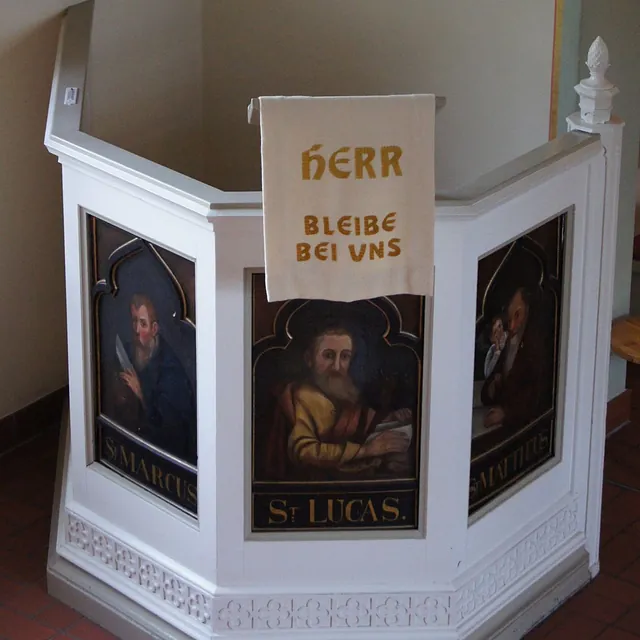 Weiße Kanzel von 1839 aus der Spandauer Nikolaikirche mit gemalten Evangelistenbildern und dem Behang „Herr bleibe bei uns“