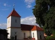 Dorfkirche Alt-Staaken von außen: weißer Bau mit Turm und rotem Ziegeldach unter blauem Himmel
