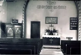 Historische Schwarz-Weiß-Aufnahme des Kirchraums mit Bankreihen, Altar, Kanzel und Wandinschrift