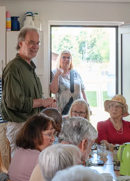 Menschen aus der Gemeinde sitzen und stehen im Gespräch an einem Tisch während einer Veranstaltung im Gemeindehaus.