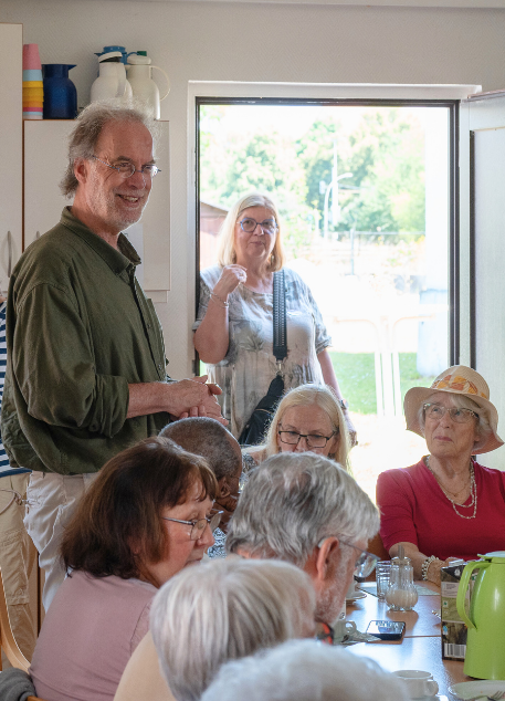 Menschen aus der Gemeinde sitzen und stehen im Gespräch an einem Tisch während einer Veranstaltung im Gemeindehaus.