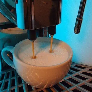 Eine Kaffeemaschine füllt einen Cappuccino in eine weiße Tasse