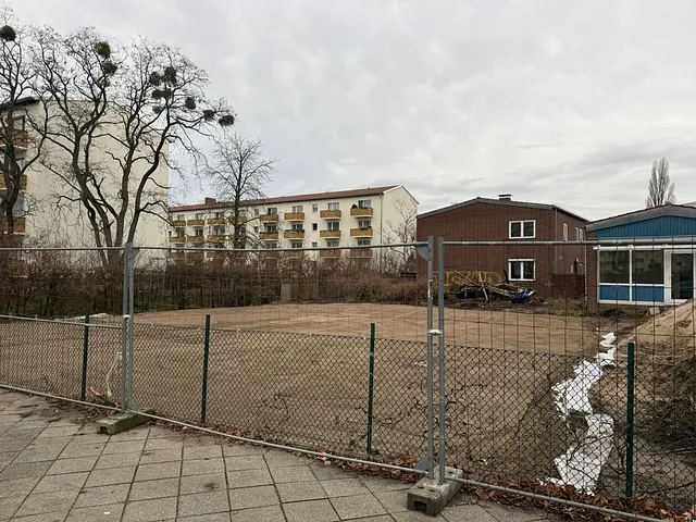 Gelände der ehemaligen Zuversichtskirche am Brunsbütteler Damm hinter einem Bauzaun, im Hintergrund Gebäude des alten Ensembles (Januar 2025)