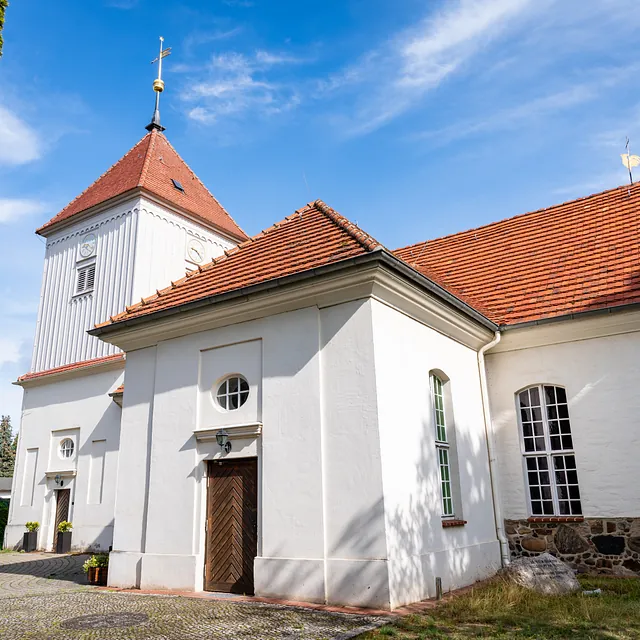 Schrägansicht der Dorfkirche Alt-Staaken mit Turm und rotem Dach vor blauem Himmel