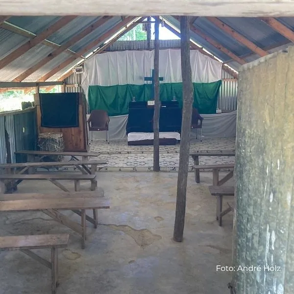 Ein einfacher Kirchenraum mit Holzbänken und Altarbereich unter einem offenen Dach.