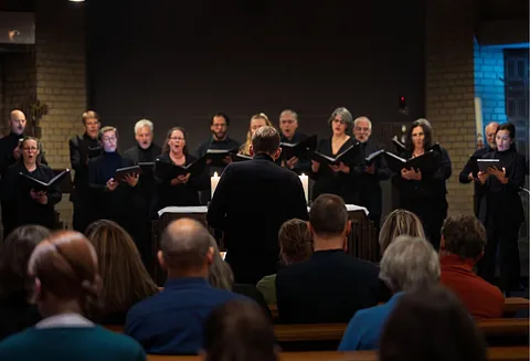 Ein Chor aus Frauen und Männern singt, im Vordergrund sitzt Publikum