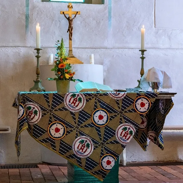 Altar der Dorfkirche mit buntem Altartuch, Kruzifix, Kerzen und Blumen